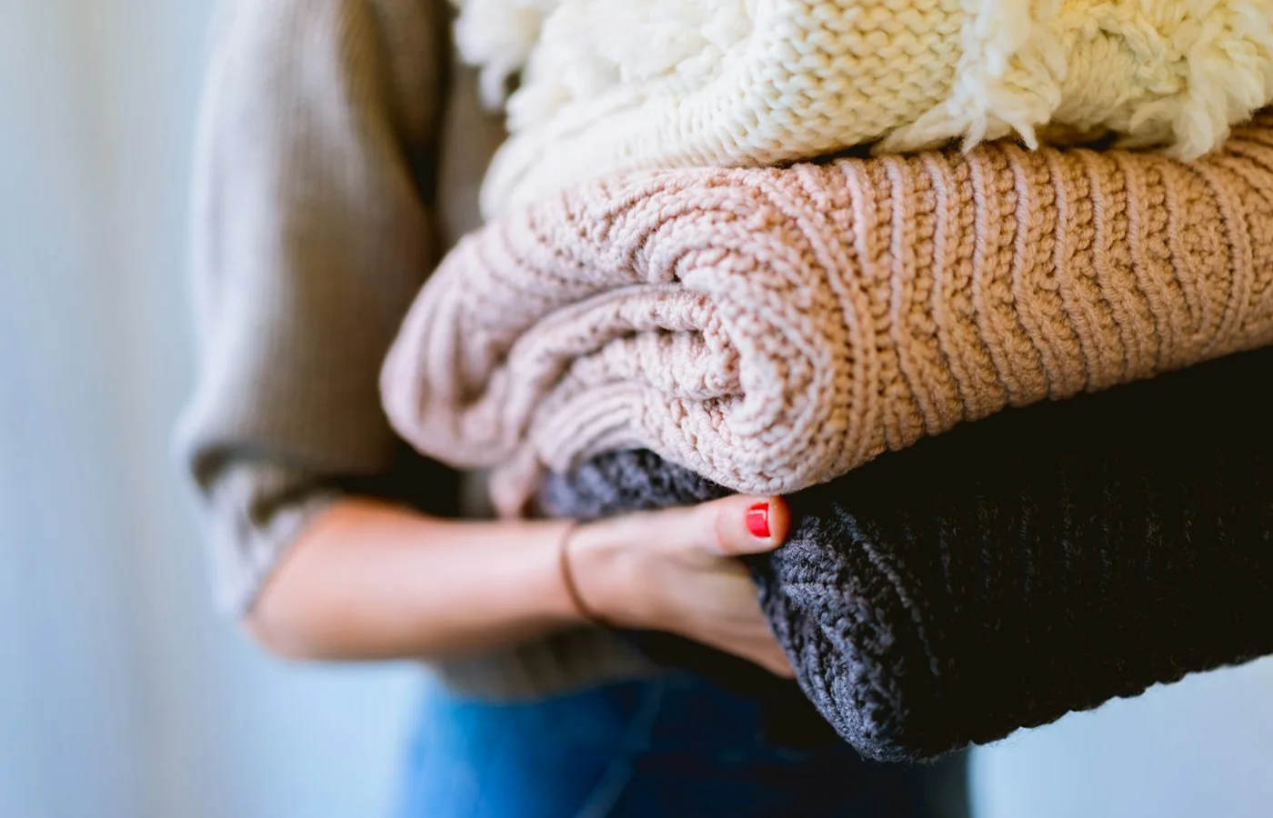 Person trägt einen Stapel gefalteter Strickkleidung